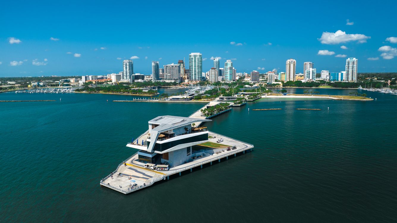 Aerial drone view of The Vinoy's pink Mediterranean Revival silhouette on the St. Petersburg downtown waterfront, with Tampa Bay beyond.